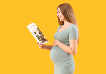 Beautiful young happy pregnant woman reading magazine on yellow background