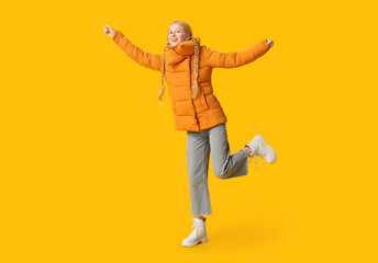 Beautiful young happy woman in warm winter clothes on yellow background