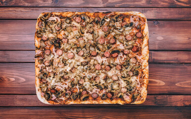 Homemade pizza with sausages, mushrooms, cheese and onions lies on a mahogany table. The concept of...