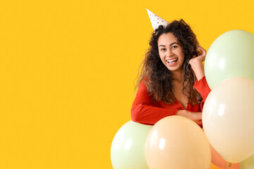 Beautiful young African-American woman in party hat with air balloons celebrating Birthday on yellow background - Powered by Adobe