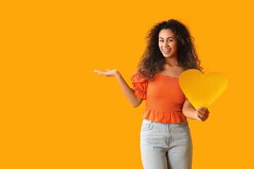 Beautiful young African-American woman with yellow paper heart on color background