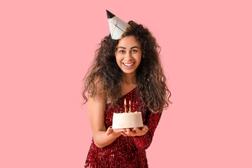 Beautiful young African-American woman in party hat with sweet cake celebrating Birthday on pink background