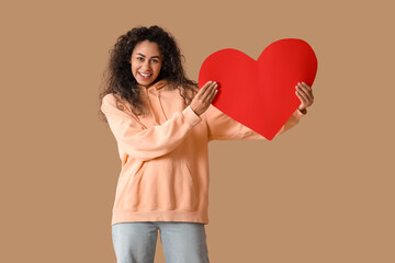 Beautiful young African-American woman with red paper heart on brown background