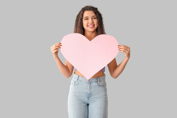 Happy young woman with pink paper heart on grey background
