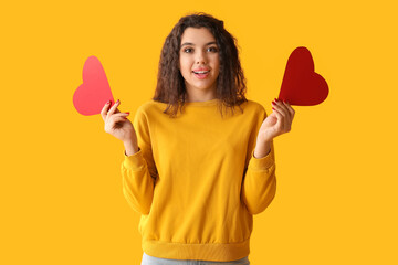 Beautiful young woman with red paper hearts on yellow background