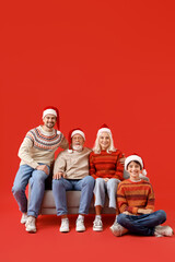 Happy family in Santa hats sitting on sofa against red background