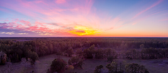 Aerial view of a beautiful Sunset with a bright orange sun, pink and purple clouds and a red hue over the treetops in Rural Texas