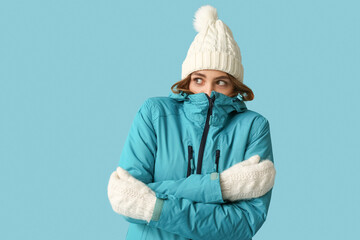 Frozen young woman in warm winter clothes on blue background