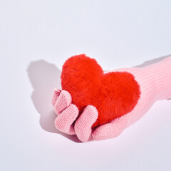 A woman's hand in a woolen glove holds a fur heart, the idea of ​​care, love, kindness.