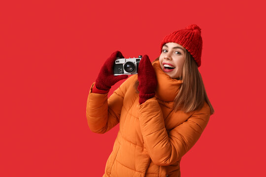 Beautiful young woman in warm winter clothes with camera on red background