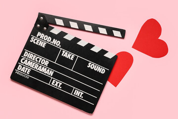 Naklejka premium Movie clapper and paper hearts on pink background. Valentine's Day celebration