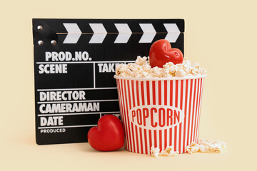 Movie clapper with bucket of popcorn and hearts on yellow background. Valentine's Day celebration