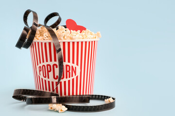 Bucket of popcorn with film reel and paper heart on blue background. Valentine's Day celebration