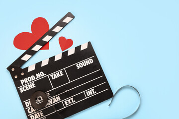 Movie clapper with film reel and paper hearts on blue background. Valentine's Day celebration