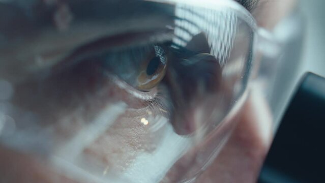 Extreme close-up view of scientist in protective glasses looking into microscope in laboratory
