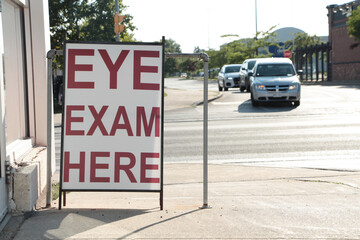 eye exam here writing text caption sandwich board sign in front of store with road behind, lined up...