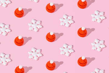Winter holidays creative pattern, snowflakes and Santa Claus hats on pastel pink background.