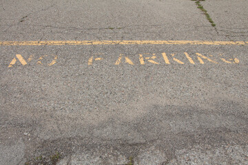no parking caption print text writing in yellow below line on pavement, worn and faded, shot straight on looking down top of frame © Penguin