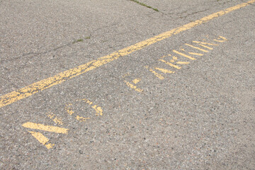 no parking caption print text writing in yellow below line on pavement, worn and faded, shot on...