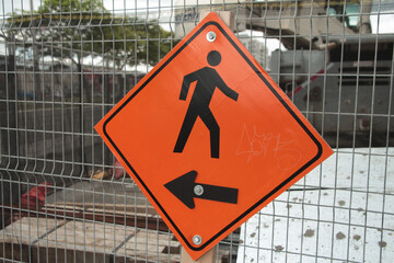 diamond orange sign with arrow pointing left and illustration of person walking right in black...