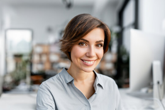 Portrait einer jungen Frau mit braunen Augen und kurzen dunklen Haaren die zuhause im Home Office B&uuml;ro in die Kamera l&auml;chelt