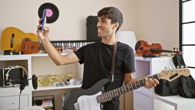 Smiling young hispanic man, a rockstar musician, electrifies the room making a selfie with his electric guitar in a music studio