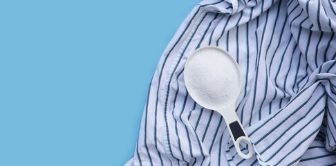 Detergent powder in measuring spoon on cloth before washing. Laundry concept.