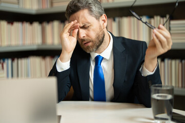 Headache, tiredness and stress. Business man in suit uses a laptop, is tired got headache migraine. Headache pain concept. Painful men are stressed at work in office. Stressful and headache.