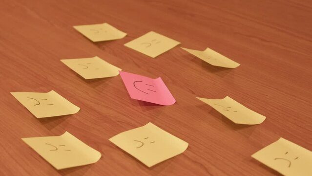 Sad faces on yellow sticky notes with one pink happy one. High quality 4k footage