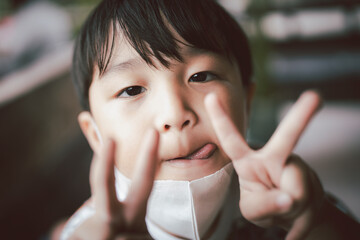 A Asian boy holds up two fingers, sticks out his tongue and makes a funny face.