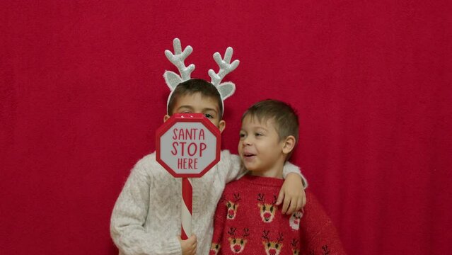 Cute kids brothers hugging and showing santa stop here sign. Christmas celebration and happy family. High quality 4k footage