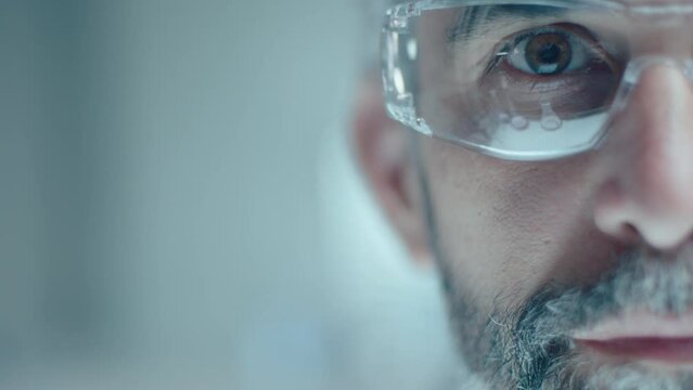Half of face of senior lab chemist in protective eyeglasses looking at camera. Extreme close up shot with copy space