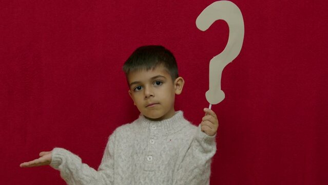 Cute child questioning something. Holding question mark , isolated on red with copy space. Slow motion. High quality 4k footage