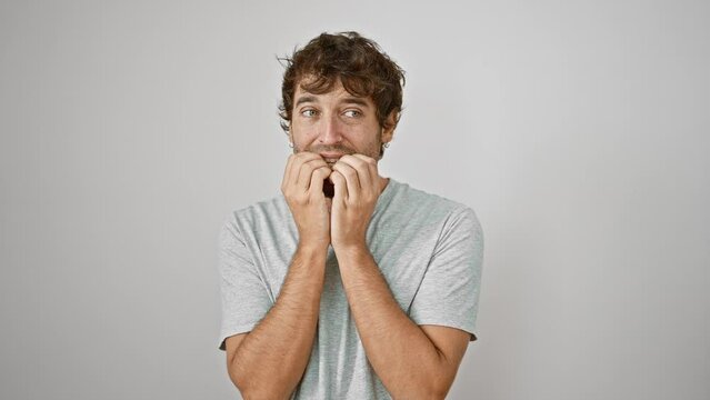 Stressed young man in white t-shirt, apprehensive and biting his nails, isolated on a white background, symbolizing anxiety problems and fear.