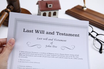 Woman holding last will and testament at white table, closeup