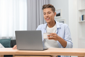Happy young man having video chat via laptop at wooden table indoors