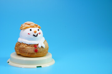 Snowman Choux Cream isolated on blue background. Choux pastry snowman, Ideas for Christmas food, DIY, Do It Yourself. Greeting card for Christmas and New year, copy space for Text