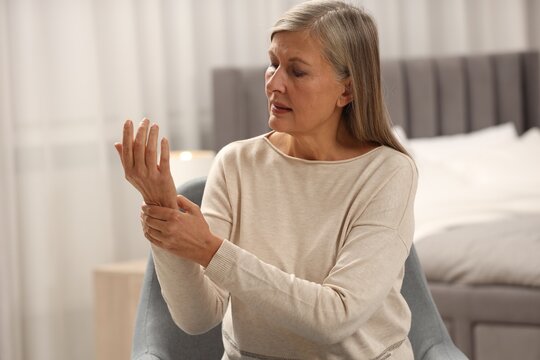 Mature woman suffering from pain in hand at home, space for text. Rheumatism symptom
