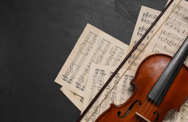 Violin, bow and music sheets on black table, top view. Space for text