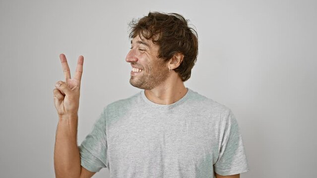 Upbeat, confident young man in a casual t-shirt, joyfully displaying the number two with his fingers, a bright smile across his face as he stands against a stark white, isolated background