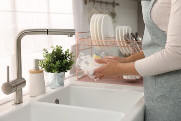 Woman washing glass at sink in kitchen, closeup