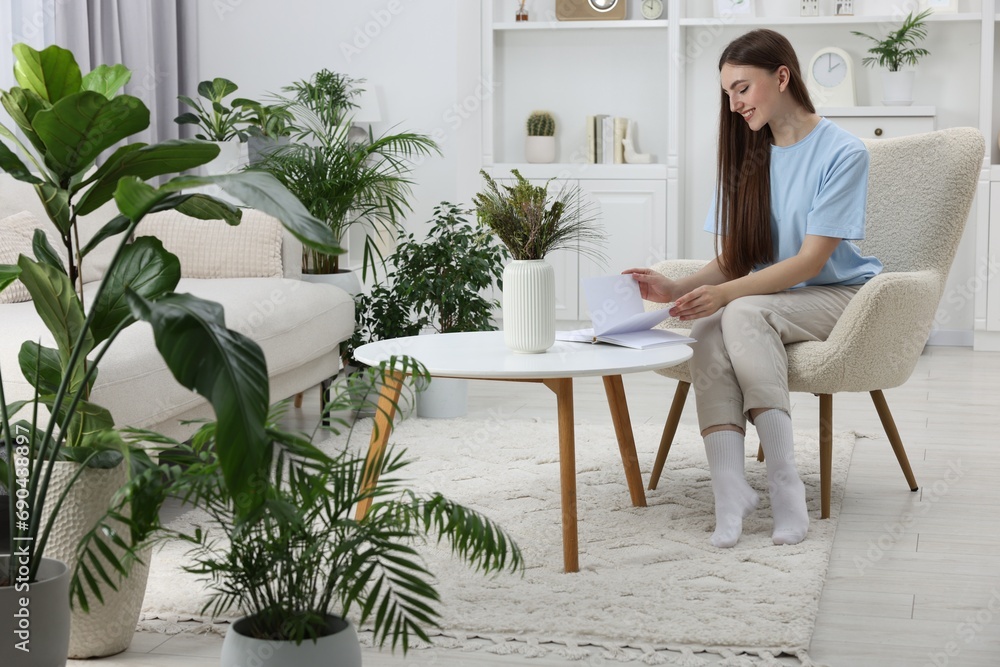 Wall mural Beautiful young woman with book at table in room with green houseplants