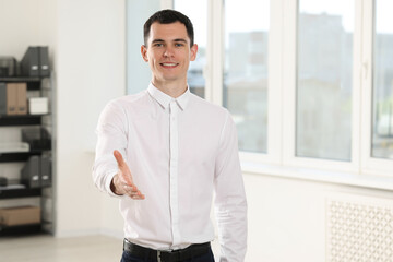 Happy man welcoming and offering handshake in office, space for text