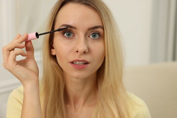 Fototapeta premium Beautiful woman applying mascara with brush indoors, closeup
