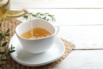 Pouring aromatic eucalyptus tea into cup on white wooden table. Space for text