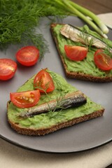 Delicious sandwiches with sprats, tomatoes, avocado puree and dill on table, closeup