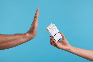 Stop smoking concept. Man refusing cigarettes on light blue background, closeup