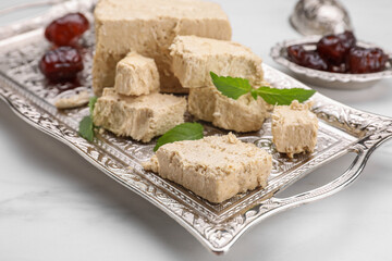 Pieces of tasty halva, dates and mint leaves on white marble table, closeup