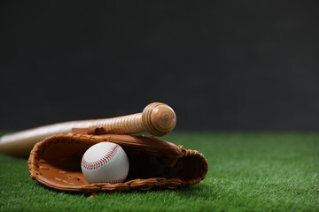 Baseball bat, leather glove and ball on green grass against dark background. Space for text