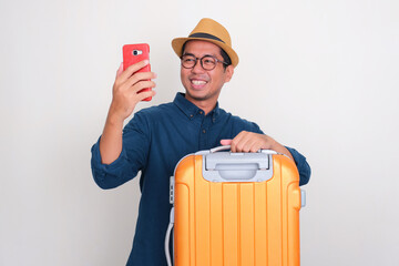 A tourist with luggage smiling happy while looking to his mobile phone